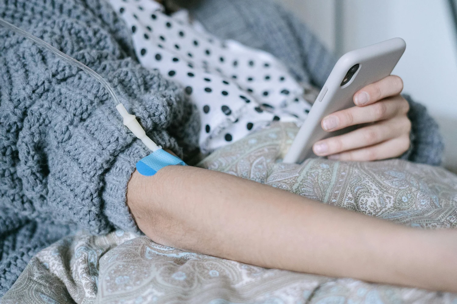 Patient with an IV line in their arm using a mobile phone