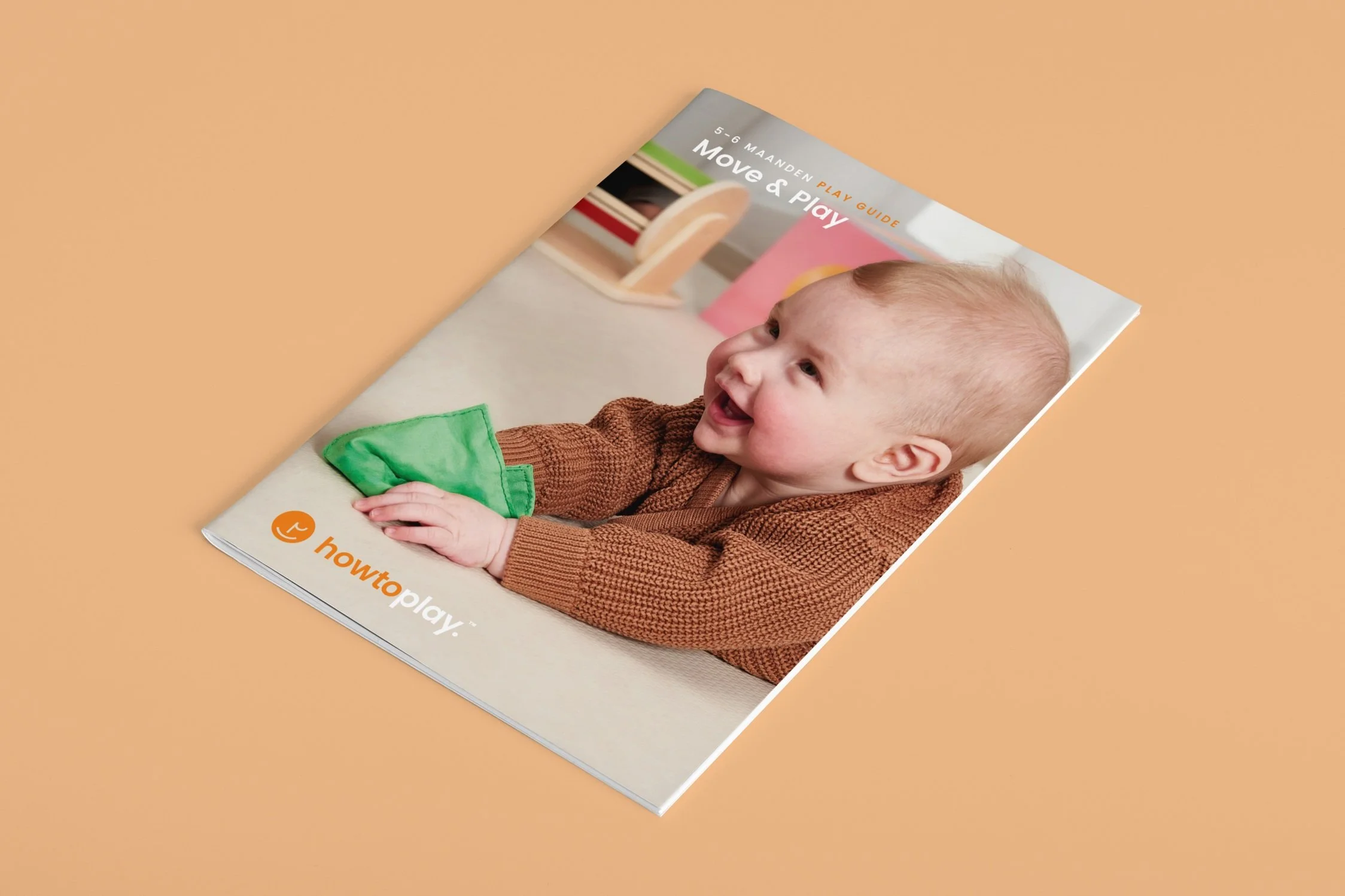 Cover of the Move & Play guide for 5 to 6 months, from a Howtoplay play box, showing a smiling baby holding a green cloth